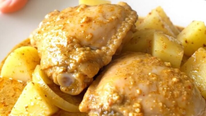 A stainless steel slow cooker filled with raw bone-in chicken thighs, potato cubes, and onion wedges.