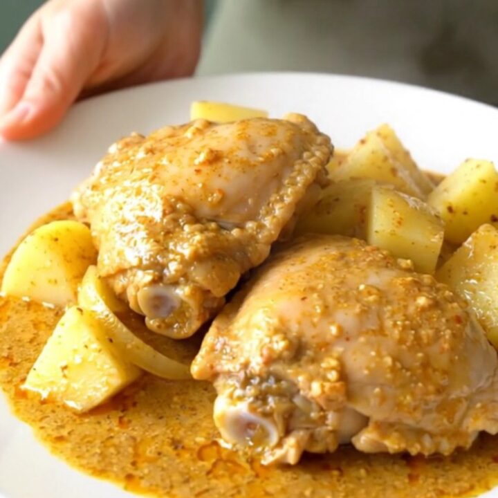 A stainless steel slow cooker filled with raw bone-in chicken thighs, potato cubes, and onion wedges.
