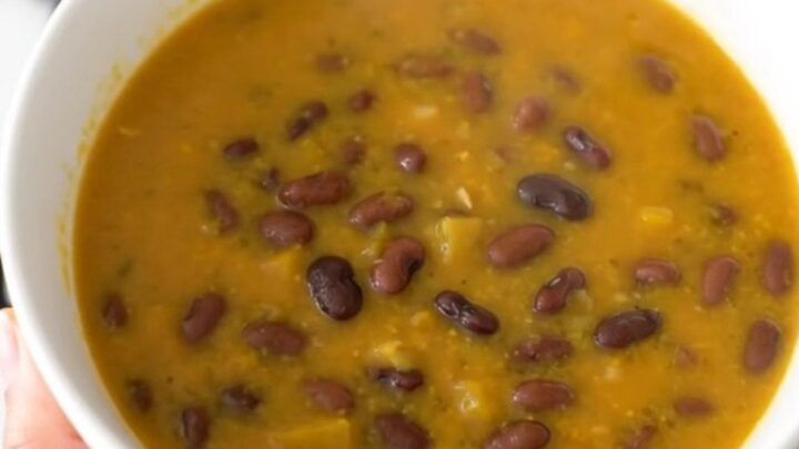 A black ceramic slow cooker filled with a rich, orange-hued pumpkin and black bean soup.