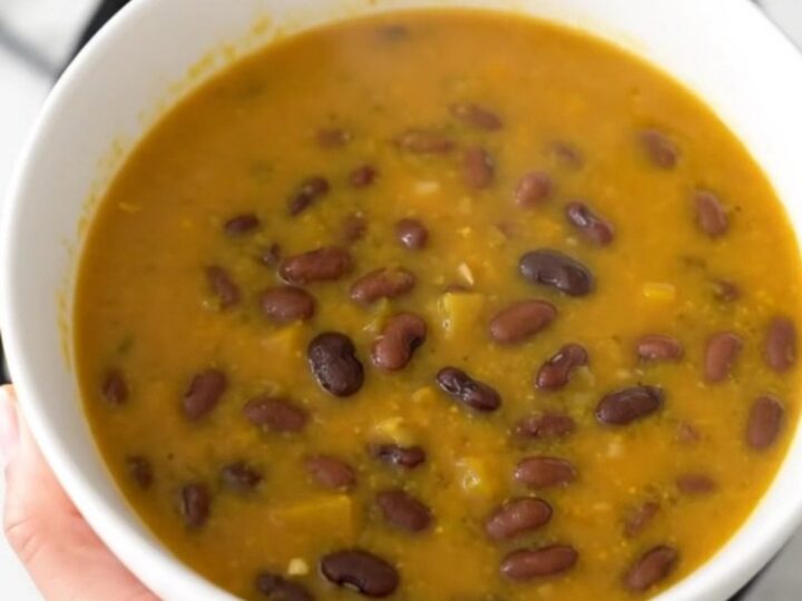 A black ceramic slow cooker filled with a rich, orange-hued pumpkin and black bean soup.
