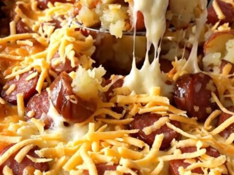 A top-down view of a rectangular baking dish filled with raw diced red potatoes and sliced andouille sausage