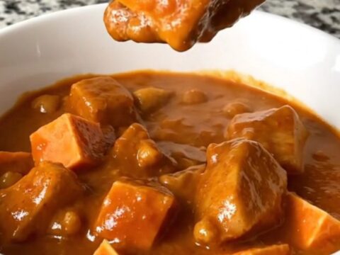 A top-down view of a slow cooker filled with a rich, peanut-based chicken and sweet potato stew.