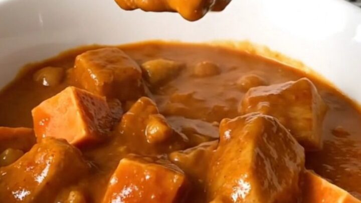 A top-down view of a slow cooker filled with a rich, peanut-based chicken and sweet potato stew.