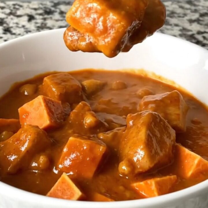 A top-down view of a slow cooker filled with a rich, peanut-based chicken and sweet potato stew.