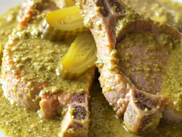 A high-angle shot of tender, braised boneless pork chops coated in a thick, creamy dill and pickle sauce in a slow cooker.