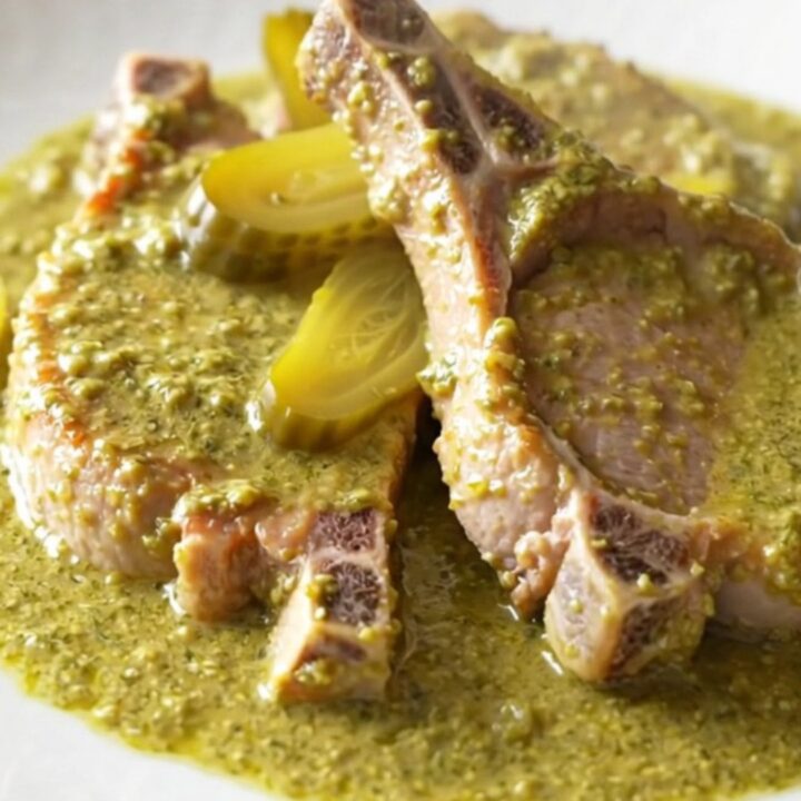 A high-angle shot of tender, braised boneless pork chops coated in a thick, creamy dill and pickle sauce in a slow cooker.
