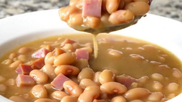 A shallow white bowl filled with creamy butter beans, tender ham cubes, and onion in a savory broth.