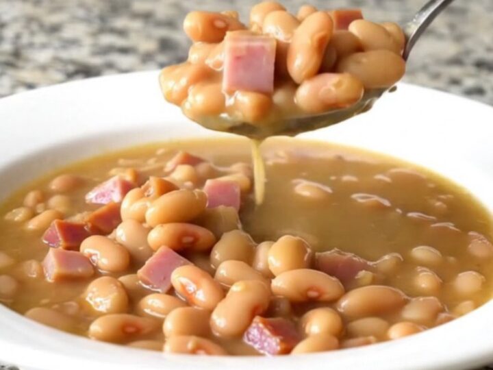 A shallow white bowl filled with creamy butter beans, tender ham cubes, and onion in a savory broth.