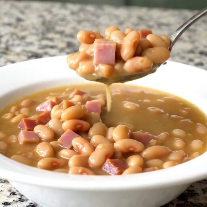 A shallow white bowl filled with creamy butter beans, tender ham cubes, and onion in a savory broth.