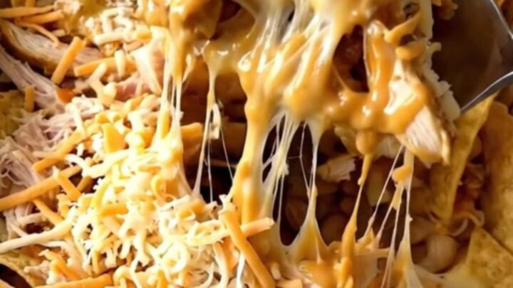 A top-down view of a rectangular baker filled with layers of tortilla chips, shredded chicken, buffalo sauce, and cheese.
