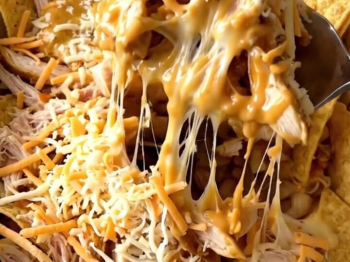 A top-down view of a rectangular baker filled with layers of tortilla chips, shredded chicken, buffalo sauce, and cheese.