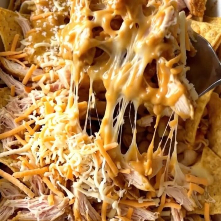 A top-down view of a rectangular baker filled with layers of tortilla chips, shredded chicken, buffalo sauce, and cheese.