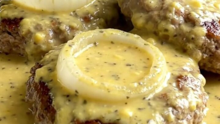 A top-down view of raw turkey burger steaks arranged in a slow cooker with onions and creamy Dijon sauce.