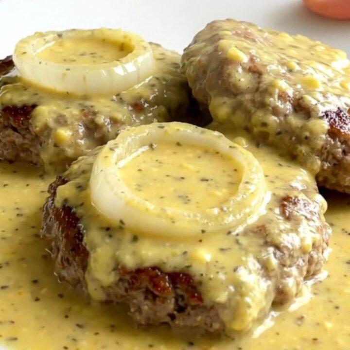 A top-down view of raw turkey burger steaks arranged in a slow cooker with onions and creamy Dijon sauce.