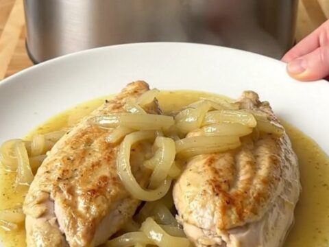 A stainless steel slow cooker filled with chicken breasts, sliced sweet onions, and a creamy Dijon mustard sauce.