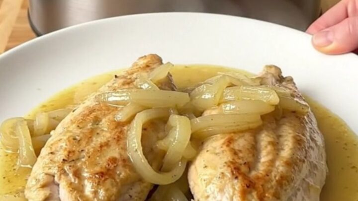 A stainless steel slow cooker filled with chicken breasts, sliced sweet onions, and a creamy Dijon mustard sauce.