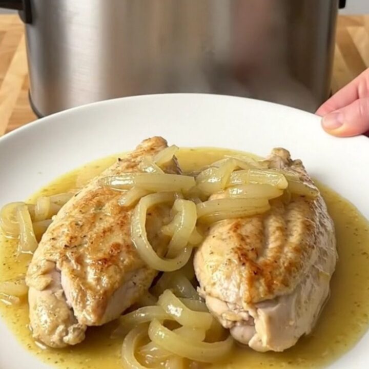 A stainless steel slow cooker filled with chicken breasts, sliced sweet onions, and a creamy Dijon mustard sauce.