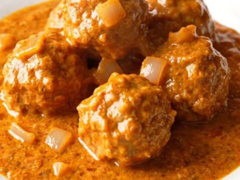 A slow cooker filled with creamy orange tikka masala turkey meatballs and onions.