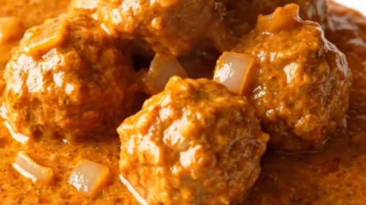 A slow cooker filled with creamy orange tikka masala turkey meatballs and onions.