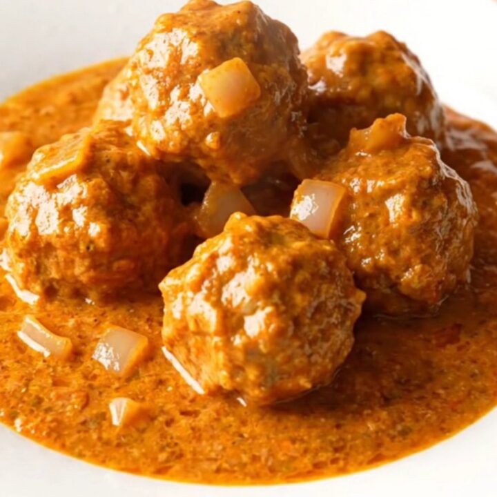 A slow cooker filled with creamy orange tikka masala turkey meatballs and onions.