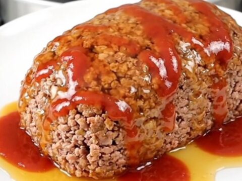 A top-down view of a raw turkey meatloaf in a black slow cooker insert, being seasoned with paprika, ketchup, and hot honey.