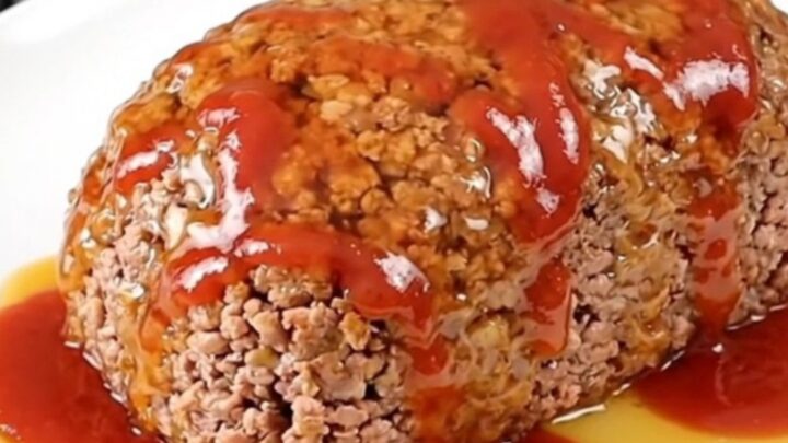 A top-down view of a raw turkey meatloaf in a black slow cooker insert, being seasoned with paprika, ketchup, and hot honey.