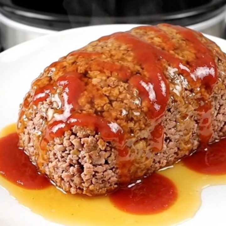 A top-down view of a raw turkey meatloaf in a black slow cooker insert, being seasoned with paprika, ketchup, and hot honey.