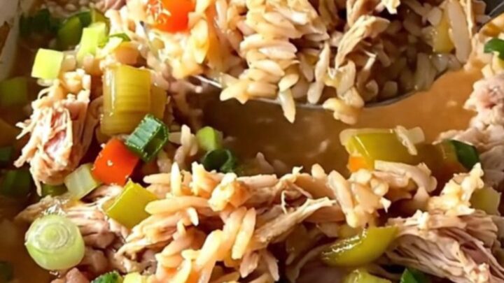 A rustic white baking dish filled with a savory Cajun dirty rice bake topped with fresh green onions.