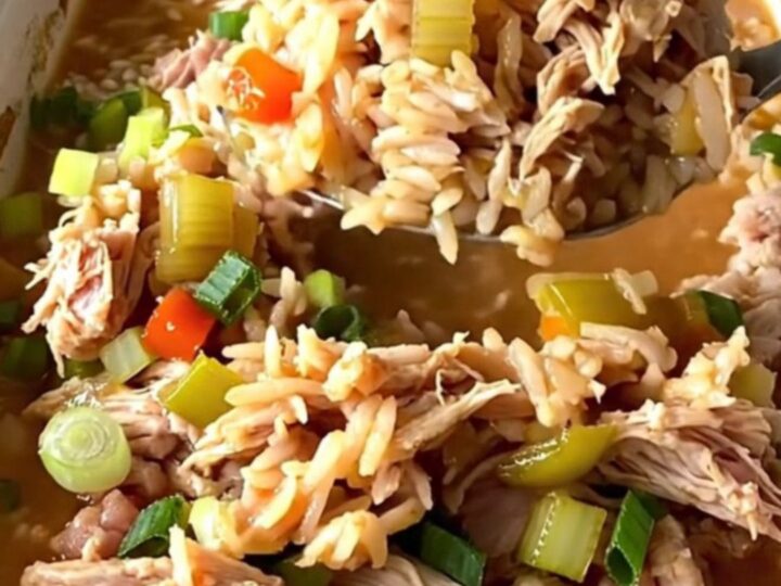 A rustic white baking dish filled with a savory Cajun dirty rice bake topped with fresh green onions.