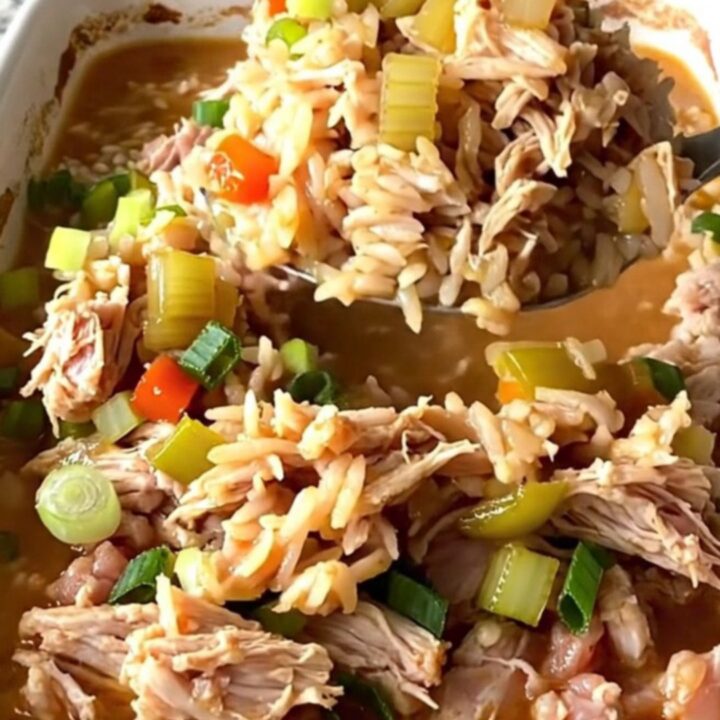 A rustic white baking dish filled with a savory Cajun dirty rice bake topped with fresh green onions.