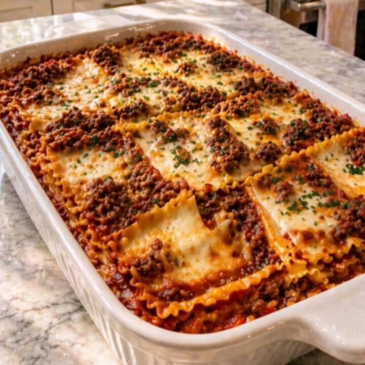 A hearty square of freshly baked beef lasagna being lifted from a white casserole dish with a spatula.