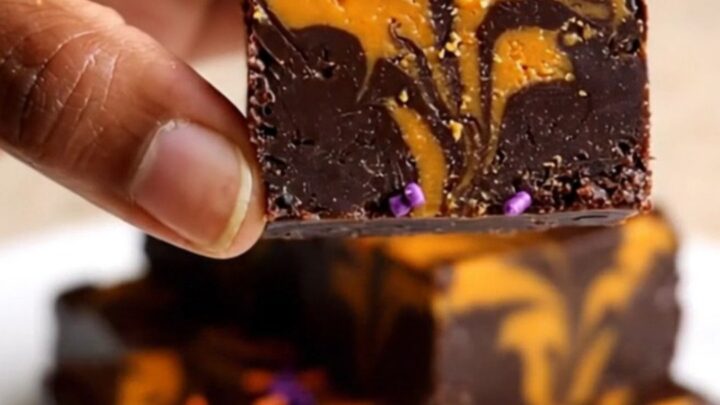 A top-down view of a thick, marbled black and orange chocolate fudge square on parchment paper.