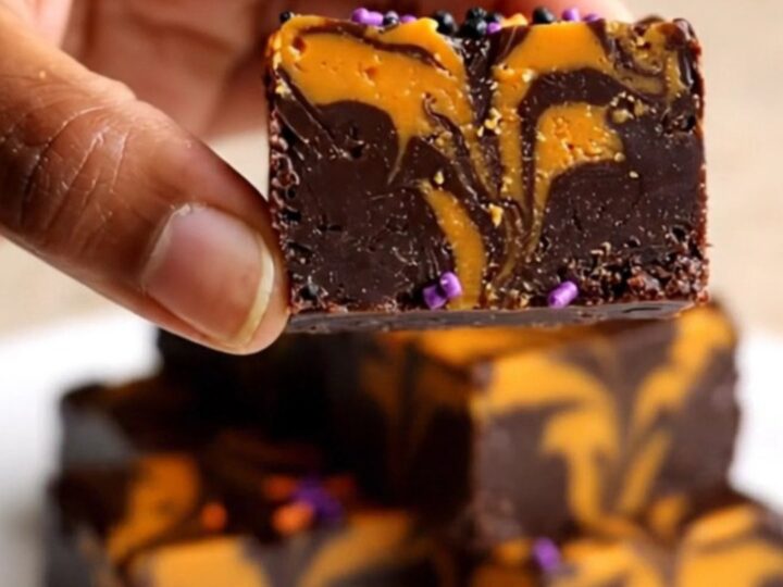 A top-down view of a thick, marbled black and orange chocolate fudge square on parchment paper.