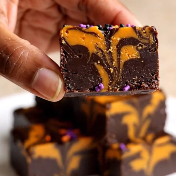 A top-down view of a thick, marbled black and orange chocolate fudge square on parchment paper.