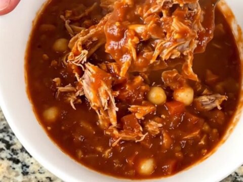 A close-up of a slow cooker filled with a hearty turkey and hominy chili in a rich red sauce.