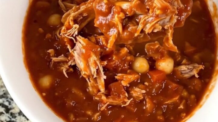 A close-up of a slow cooker filled with a hearty turkey and hominy chili in a rich red sauce.