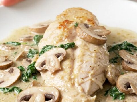 A close-up of tender chicken breasts covered in a creamy mushroom and spinach sauce in a slow cooker.