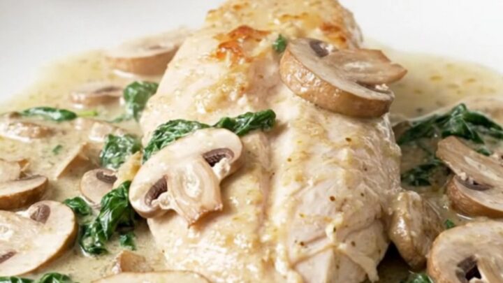 A close-up of tender chicken breasts covered in a creamy mushroom and spinach sauce in a slow cooker.