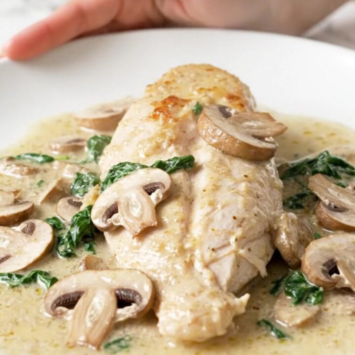 A close-up of tender chicken breasts covered in a creamy mushroom and spinach sauce in a slow cooker.