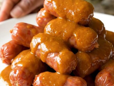 A slow cooker filled with buffalo mini smoked sausages glistening in a buttery orange sauce.