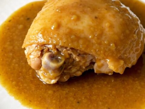 A close-up view of slow-cooked chicken thighs coated in a thick honey curry sauce with soft onions on a white plate.