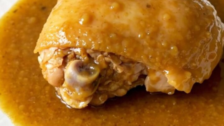 A close-up view of slow-cooked chicken thighs coated in a thick honey curry sauce with soft onions on a white plate.