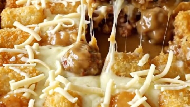 A top-down view of a rectangular baking dish filled with turkey meatballs, creamy gravy, and potato tots topped with cheese.