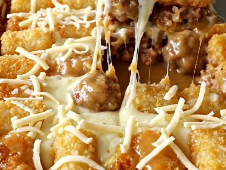 A top-down view of a rectangular baking dish filled with turkey meatballs, creamy gravy, and potato tots topped with cheese.