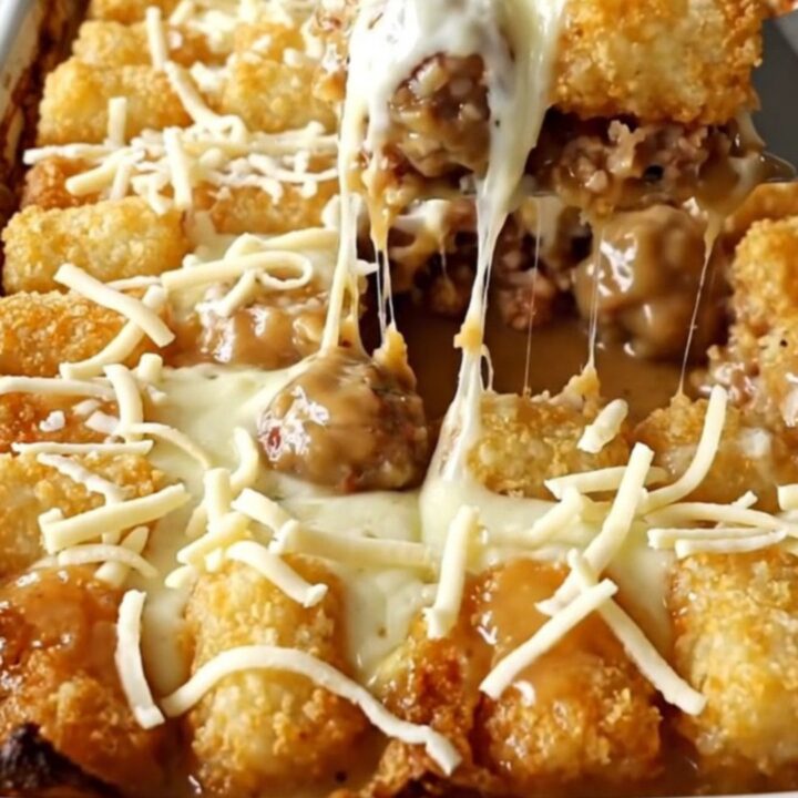 A top-down view of a rectangular baking dish filled with turkey meatballs, creamy gravy, and potato tots topped with cheese.