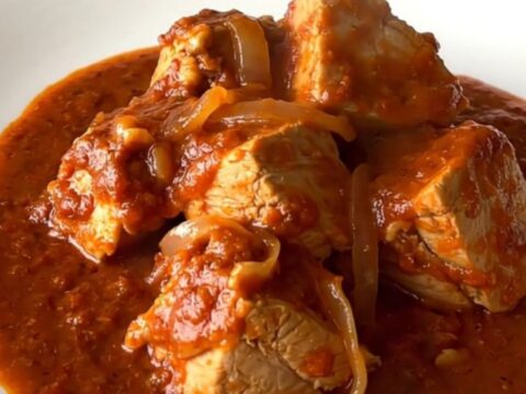 A close-up of tender chicken pieces smothered in a vibrant red chile sauce inside a black slow cooker insert.