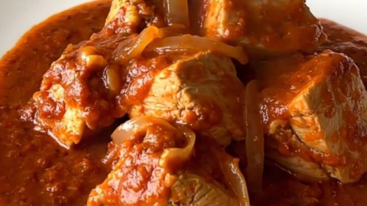 A close-up of tender chicken pieces smothered in a vibrant red chile sauce inside a black slow cooker insert.
