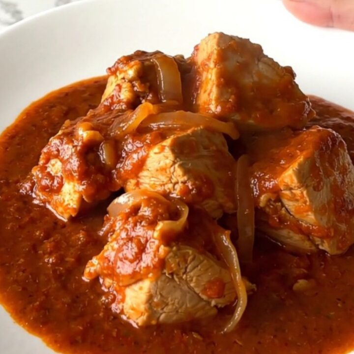 A close-up of tender chicken pieces smothered in a vibrant red chile sauce inside a black slow cooker insert.