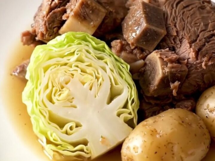 A slow cooker filled with a large chuck roast, cabbage wedges, and baby potatoes in a savory broth.