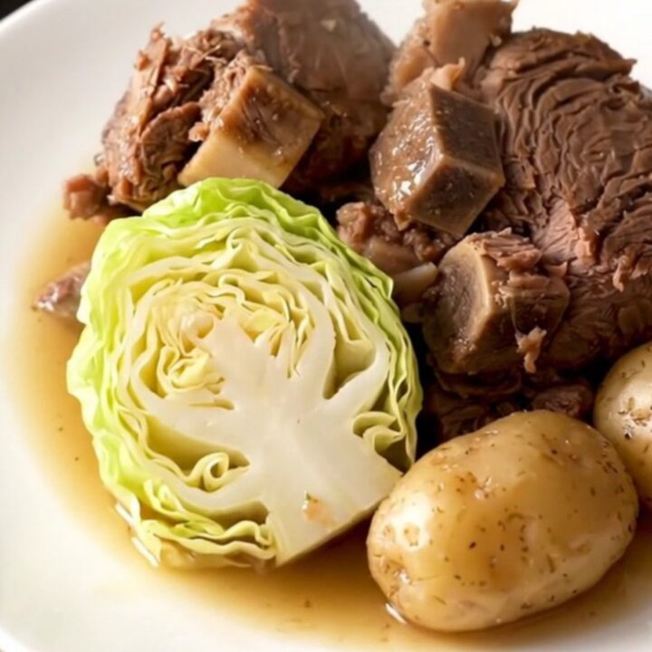 A slow cooker filled with a large chuck roast, cabbage wedges, and baby potatoes in a savory broth.